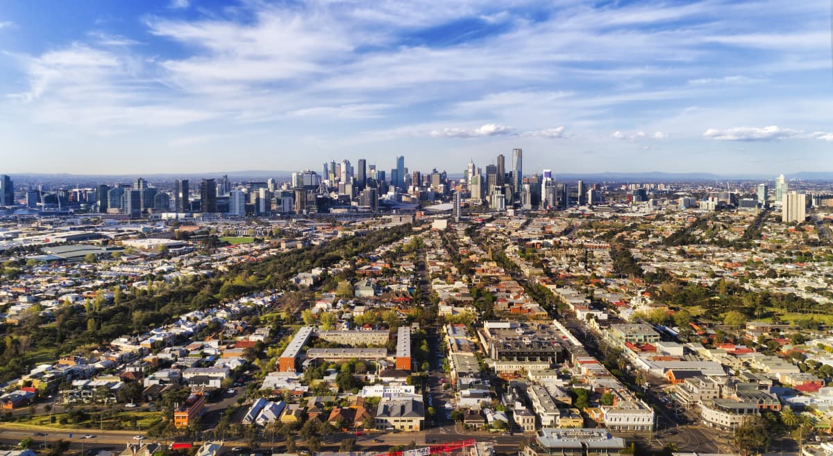 Leading streets and residential suburbs from Port Melbourne via Southbank to Melbourne city CBD against blue sky in aerial wide view.